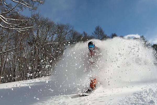 Dan riding out of a powder puff of air born snow on a bluebird day at Madarao Mountain Resort